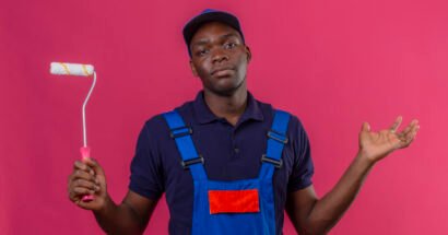 clueless young african american builder man wearing construction uniform and cap holding paint roller shrugging shoulders looking uncertain and confused having no answer spreading palms sta